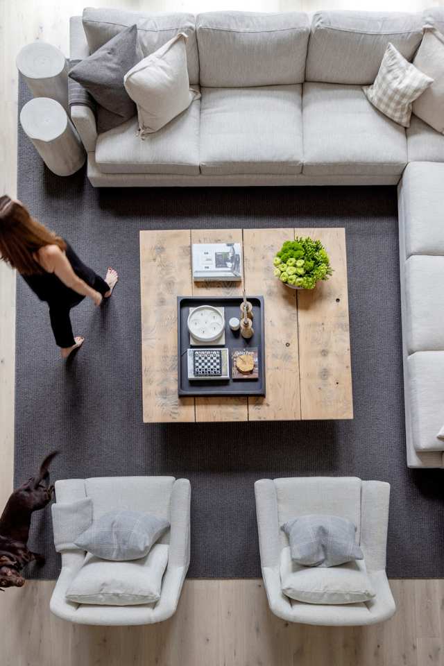 cozy living room with woman and dog walking through, beige-colored sectional couch, and wood coffee table in lake house